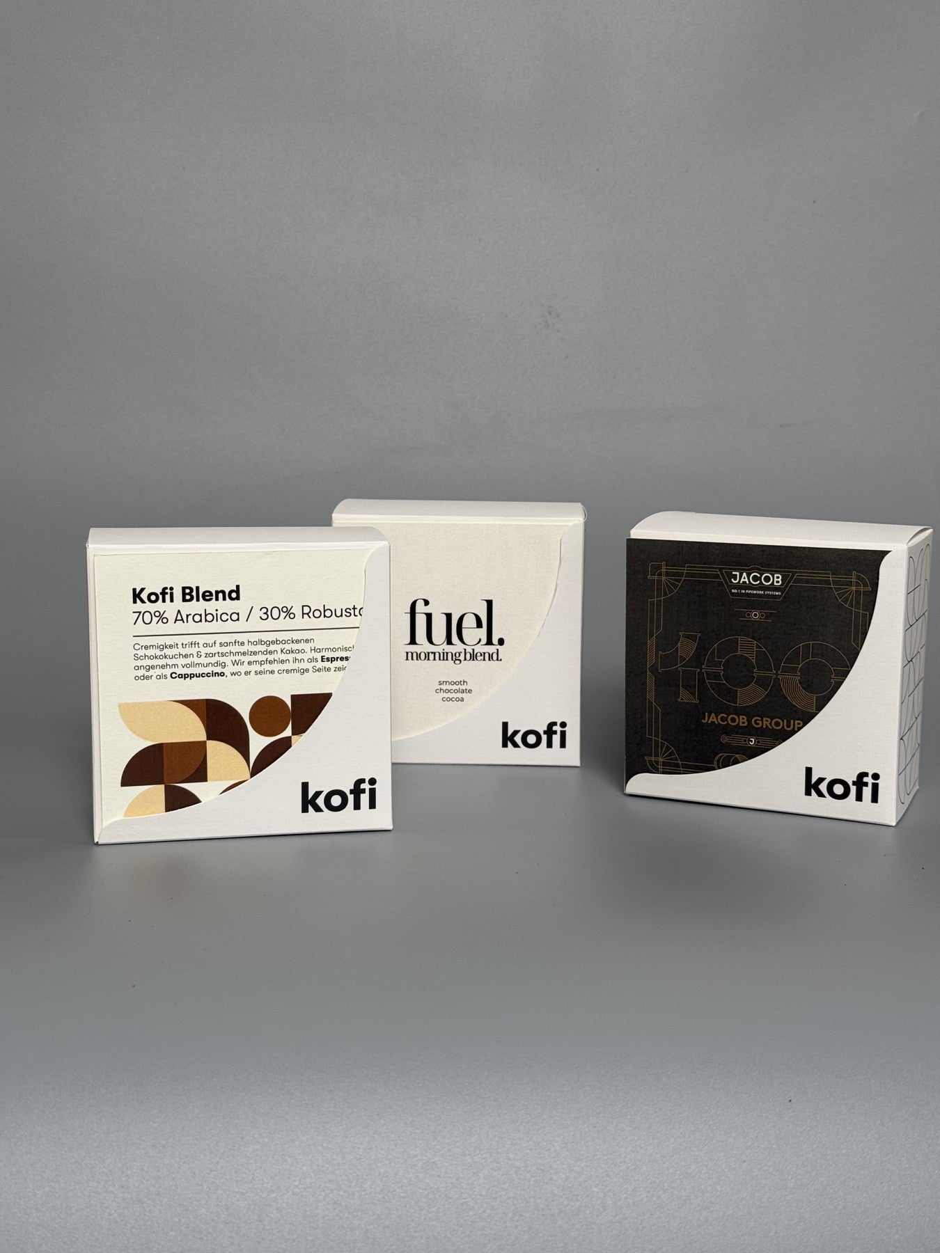 Drei echte kofi-Boxen mit unterschiedlichen Frontgestaltungen auf grauem Hintergrund